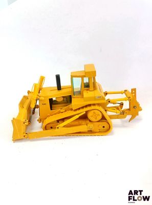un petit bulldozer jaune posé sur une surface blanche