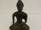 une vieille statue en bronze représentant un Bouddha assis sur un socle blanc