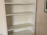 a white book shelf with a blue chair in the corner