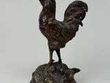statue en bronze représentant un coq posé sur un rocher, sur fond blanc