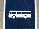 un panneau bleu et blanc représentant un bus, posé sur une surface en béton