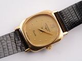 a gold watch on a black strap on a white surface