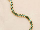 a close up of a gold and turquoise bracelet on a white surface