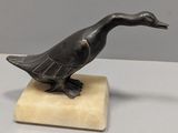 statue d'un canard posée sur un socle en marbre, sur une surface blanche