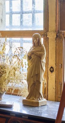 une statue représentant une femme tenant un bébé dans ses bras, posée sur une table devant une fenêtre