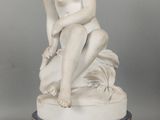 une statue blanche représentant un garçon assis sur un socle bleu