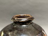 a black vase with a brown lid on a table
