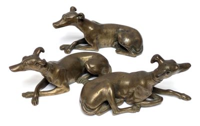 three bronze sculptures of greyhounds laying down on a white surface