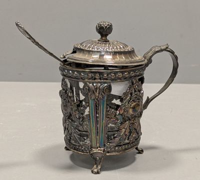 une théière en argent avec son couvercle et sa cuillère, posée sur une table