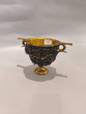 une image représentant un vase doré et noir posé sur une surface blanche