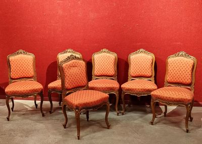 Six chaises anciennes sont alignées contre un mur rouge dans une pièce
