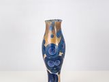 un vase bleu et or posé sur une surface blanche