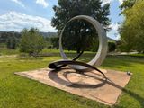 a sculpture in the middle of a grassy area with trees in the background