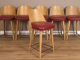 quatre tabourets de bar en bois et en cuir rouge, adossés à un mur gris