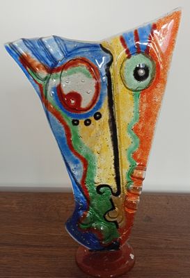 a colorful vase on a wooden table with a white wall in the background
