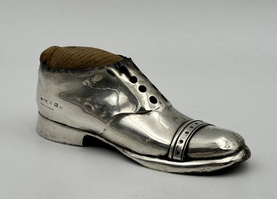 une chaussure ancienne en argent, dotée d'un talon en bois, posée sur une surface blanche