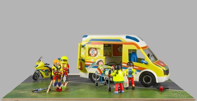 une petite maquette d'une ambulance jaune entourée d'un groupe de personnes