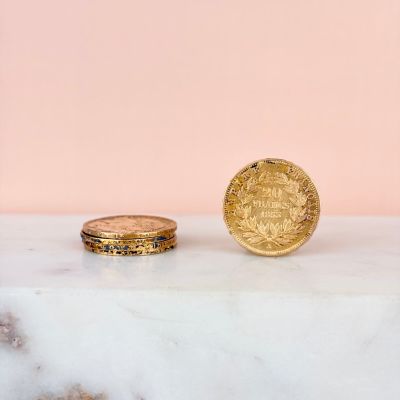 a gold coin sitting on top of a marble slab next to a gold ring