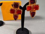 pair of red and gold earrings on a black stand next to a yellow box