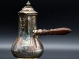 une cafetière en argent avec une poignée en bois sur un fond noir