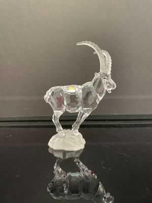 une figurine de chèvre en cristal posée sur une table en verre