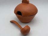a small clay teapot with a wooden spoon in it