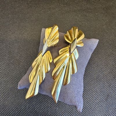 boucles d'oreilles en feuille d'or posées sur un coussin, sur fond gris