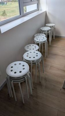 Plusieurs tabourets blancs sont alignés contre un mur dans une pièce