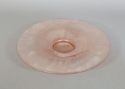 une assiette en verre rose posée sur une table, sur fond blanc