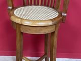 une photo d'une chaise en bois avec une assise tressée, posée sur un sol recouvert de moquette