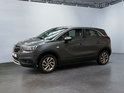 La voiture grise est garée dans une grande pièce aux murs blancs.