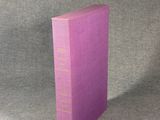 un livre violet posé sur une table près d'un mur gris