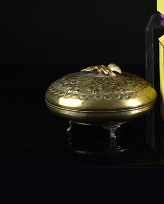 a small gold box with a gold lid next to a bottle of perfume