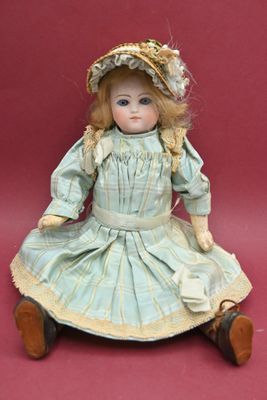 an antique doll sitting on a red surface wearing a dress and hat