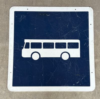 un panneau bleu et blanc représentant un bus, posé sur une surface en béton