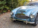 a blue sports car parked in a driveway next to a bush