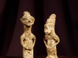 two figurines sitting on top of a wooden table next to a purple curtain