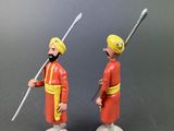 two figurines of two men in red uniforms holding swords