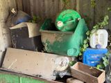 a pile of garbage in a green bin next to a wooden fence