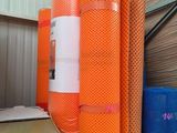 Plusieurs rouleaux de filet orange sont empilés sur des palettes dans un entrepôt