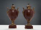 une paire de vases anciens munis d'anses, posés sur des socles, sur un fond blanc