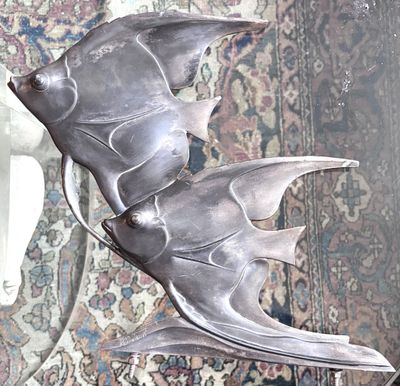 une sculpture représentant un poisson en argent, posée sur un socle devant un miroir