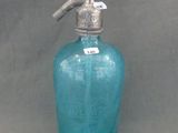 une bouteille en verre bleue munie d'une poignée en métal, sur fond gris