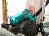 une femme tenant un aspirateur bleu et noir dans un salon