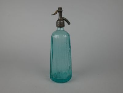 une vieille bouteille en verre bleu munie d'un bec verseur en métal, sur fond gris
