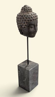statue représentant une tête de Bouddha posée sur un socle, sur fond blanc