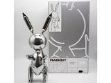 the silver rabbit is standing next to a box of scissors
