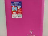 La couverture d'un cahier rose est ouverte sur une surface blanche