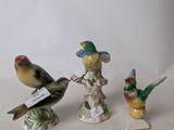 three small figurines of birds are sitting on a white surface