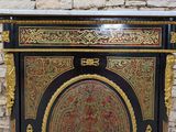 a black and gold painted cabinet on display against a brick wall